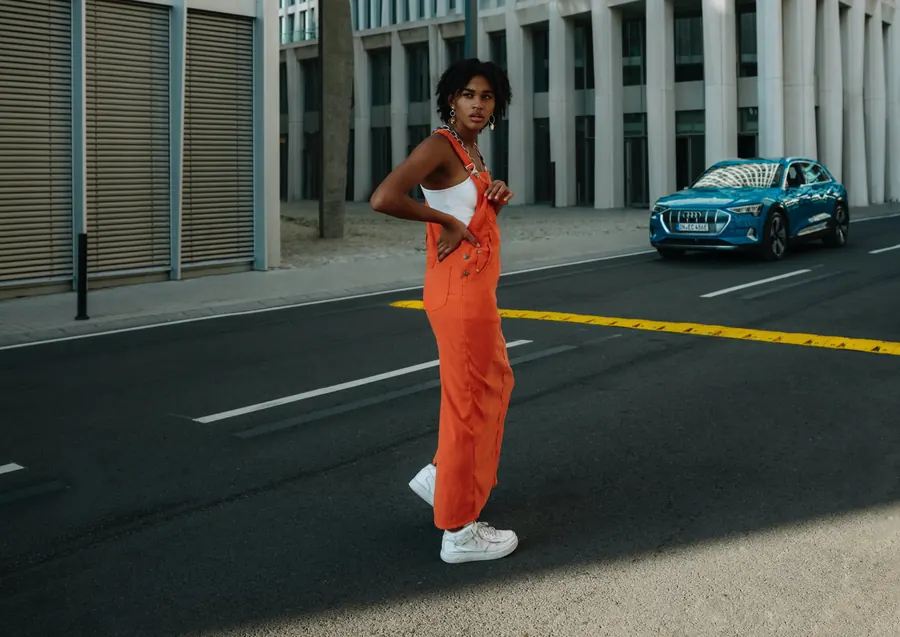 Model in Orange auf der Straße, dahinter das E-SUV